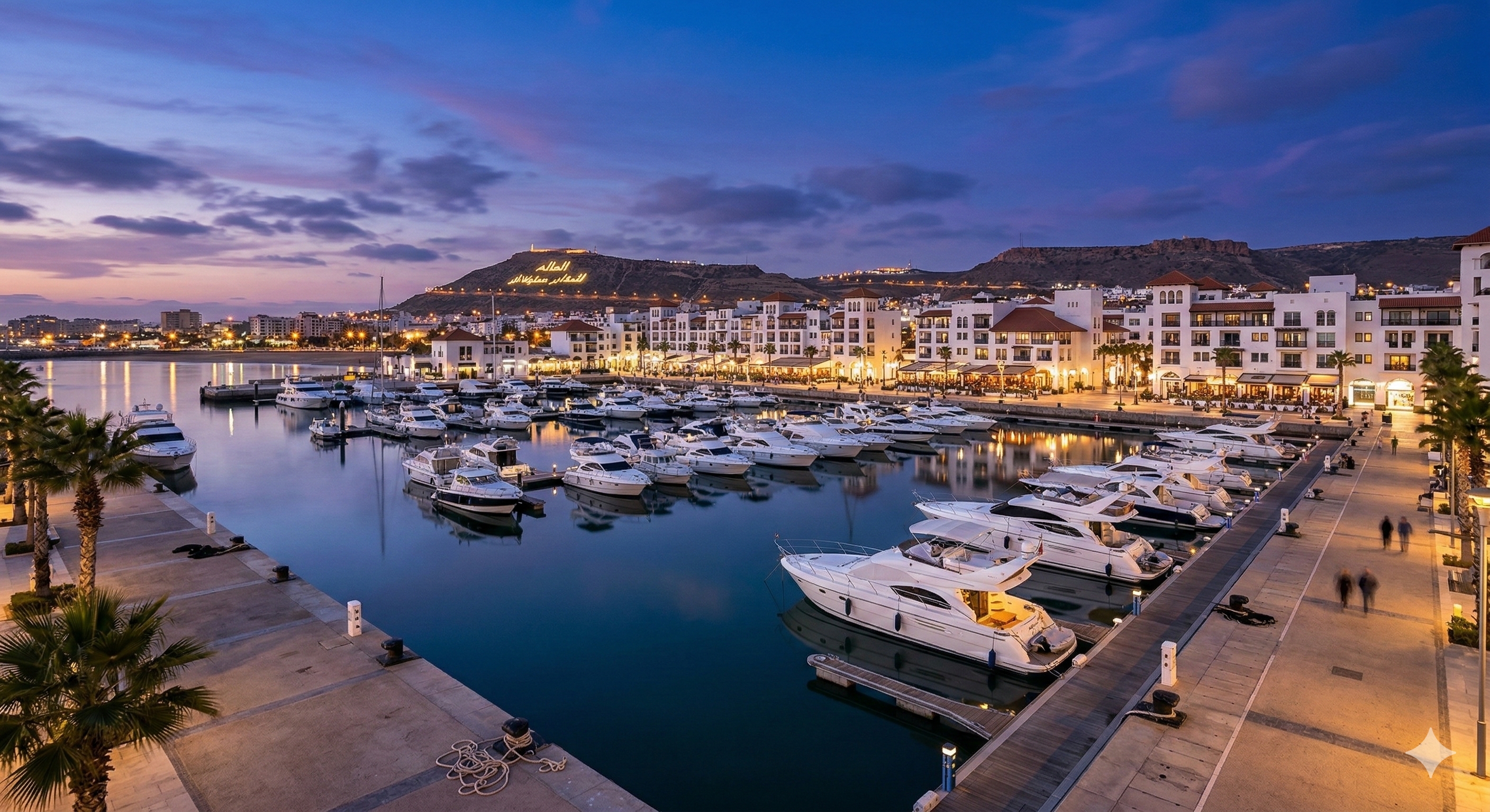 Luxury yachts docked at the Agadir Marina at dusk, featuring calm water reflections, waterfront restaurants, and a purple sunset sky