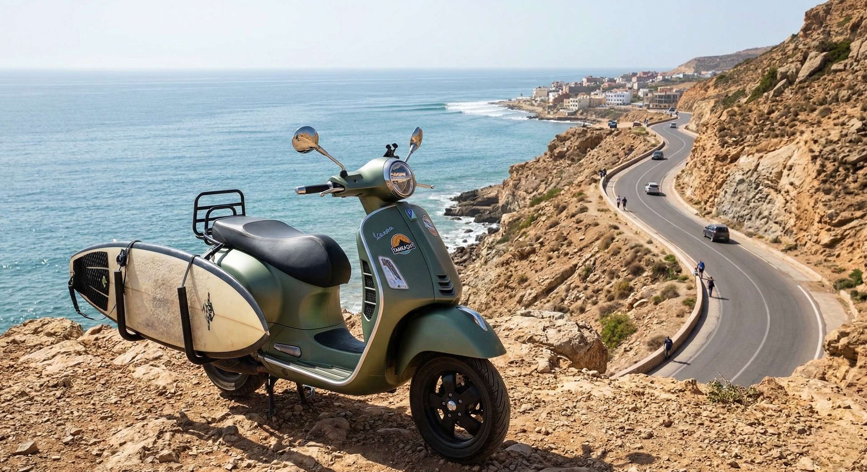 A rental scooter with a surfboard rack parked on a scenic cliff overlooking the Agadir coastline near Tamraght