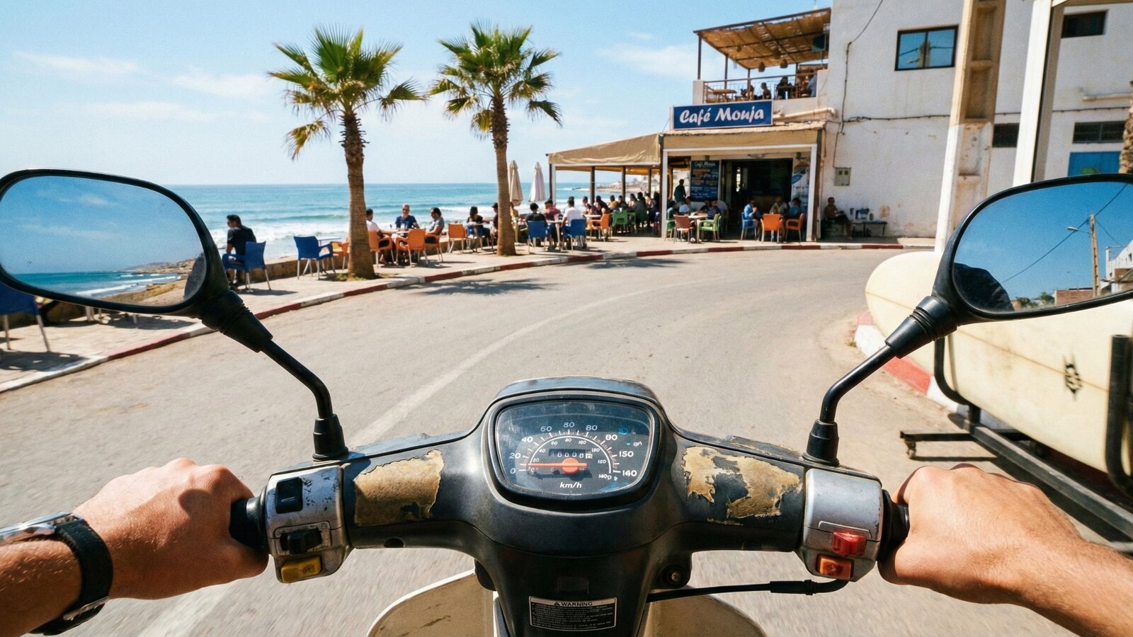 Point-of-view shot from a scooter driver's seat approaching a seaside cafe in Taghazout
